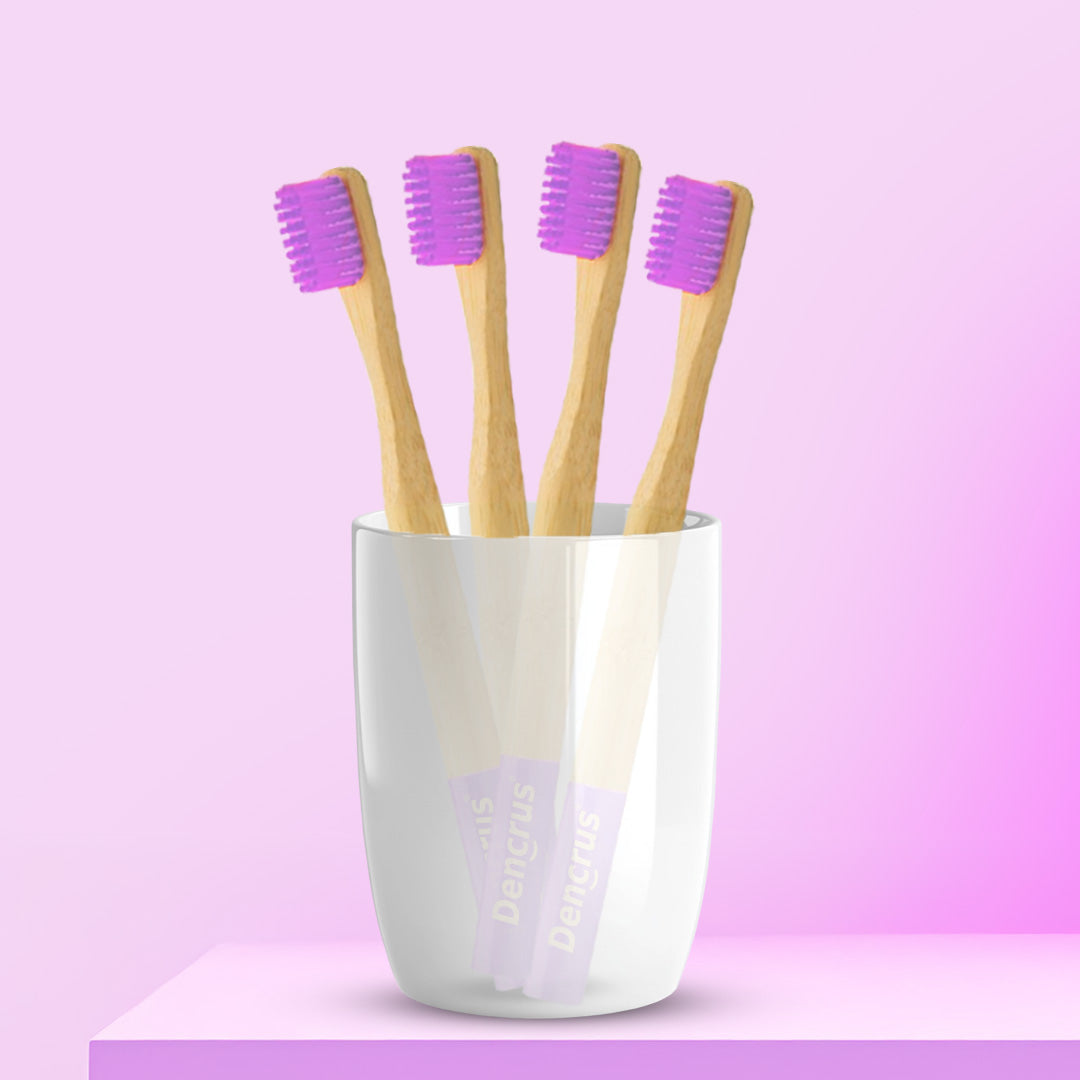 Four ORBY Kids bamboo toothbrushes with lavender bristles standing upright in a white cup, set against a pink background.