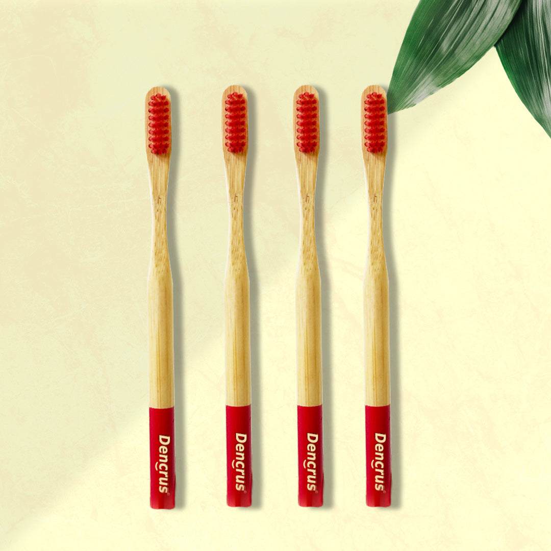 Four Dencrus ORBY Plus Red bamboo toothbrushes with red bristles and green and white branding on the handle, displayed on a beige background with a green leaf to the side.