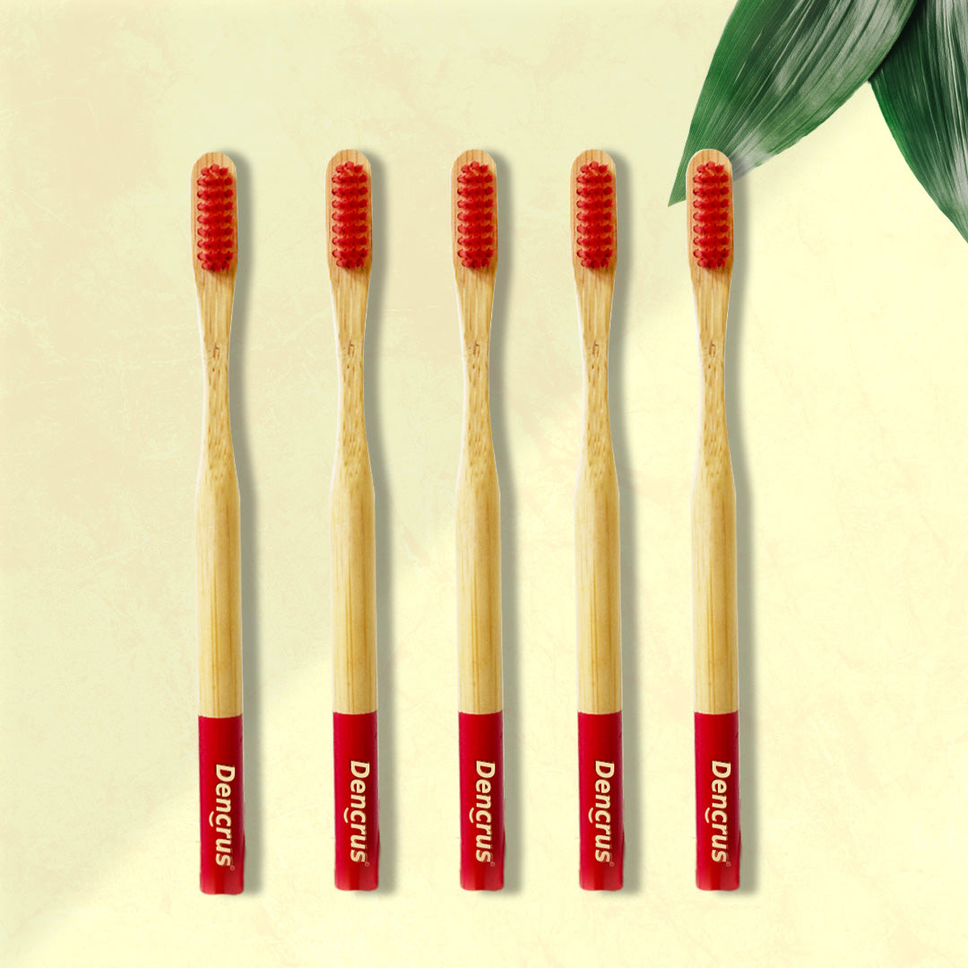 Five Dencrus RED ORBY Plus bamboo toothbrushes with red bristles and green and white branding on the handle, displayed on a beige background with a green leaf to the side.
