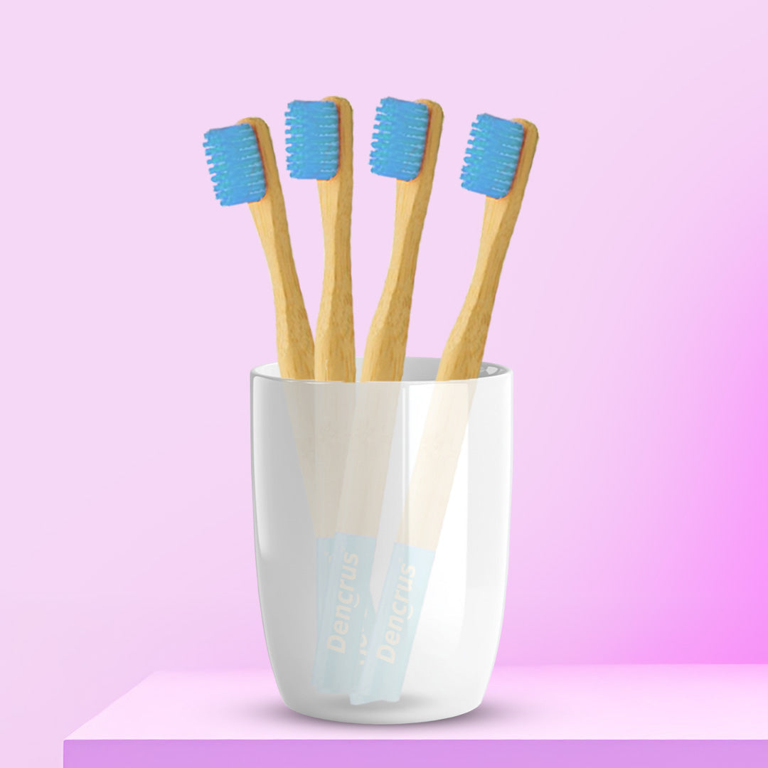 An image of four ORBY Kids bamboo toothbrushes with blue bristles standing upright in a white cup, set against a pink background.