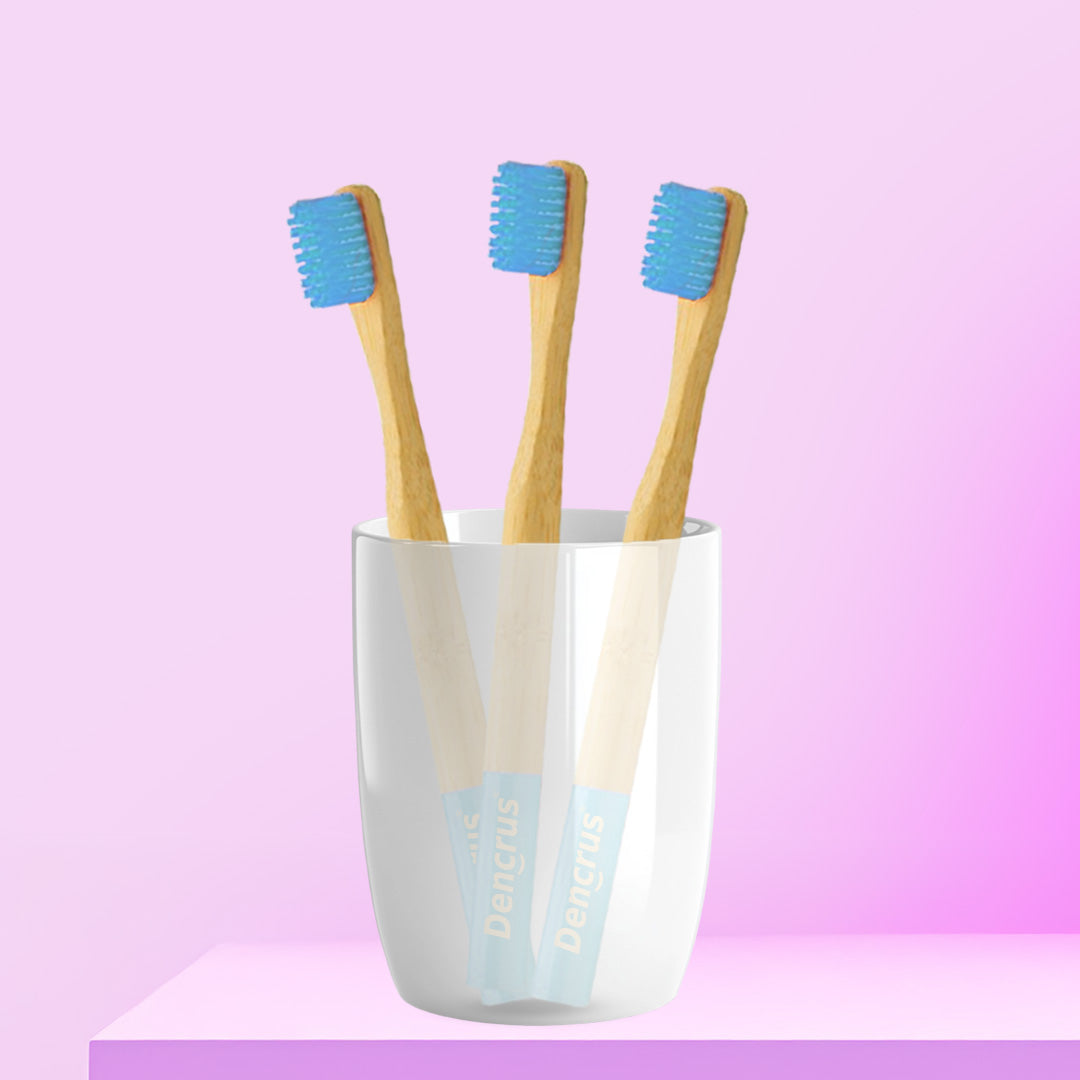 Three ORBY Kids bamboo toothbrushes with blue bristles standing upright in a white cup, set against a pink background.