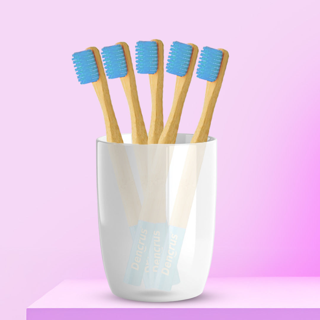 Five ORBY Kids bamboo toothbrushes with blue bristles standing upright in a white cup, set against a pink background.
