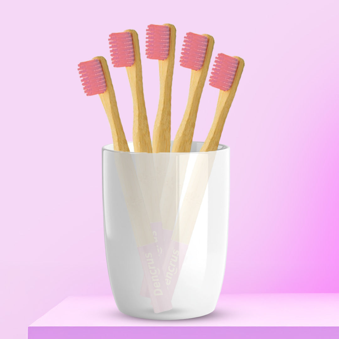 Five ORBY Kids pink bamboo toothbrushes with round handles, placed in a white cup against a pink background.