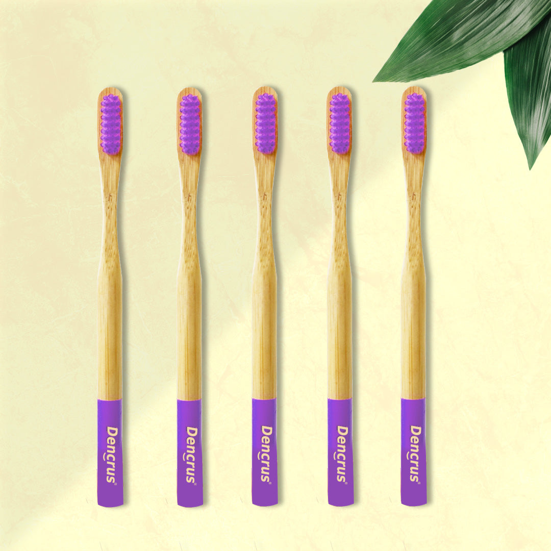 Five ORBY Plus bamboo toothbrushes with lavender-colored bristles and ergonomic handles, displayed on a beige background with a green leaf to the side.