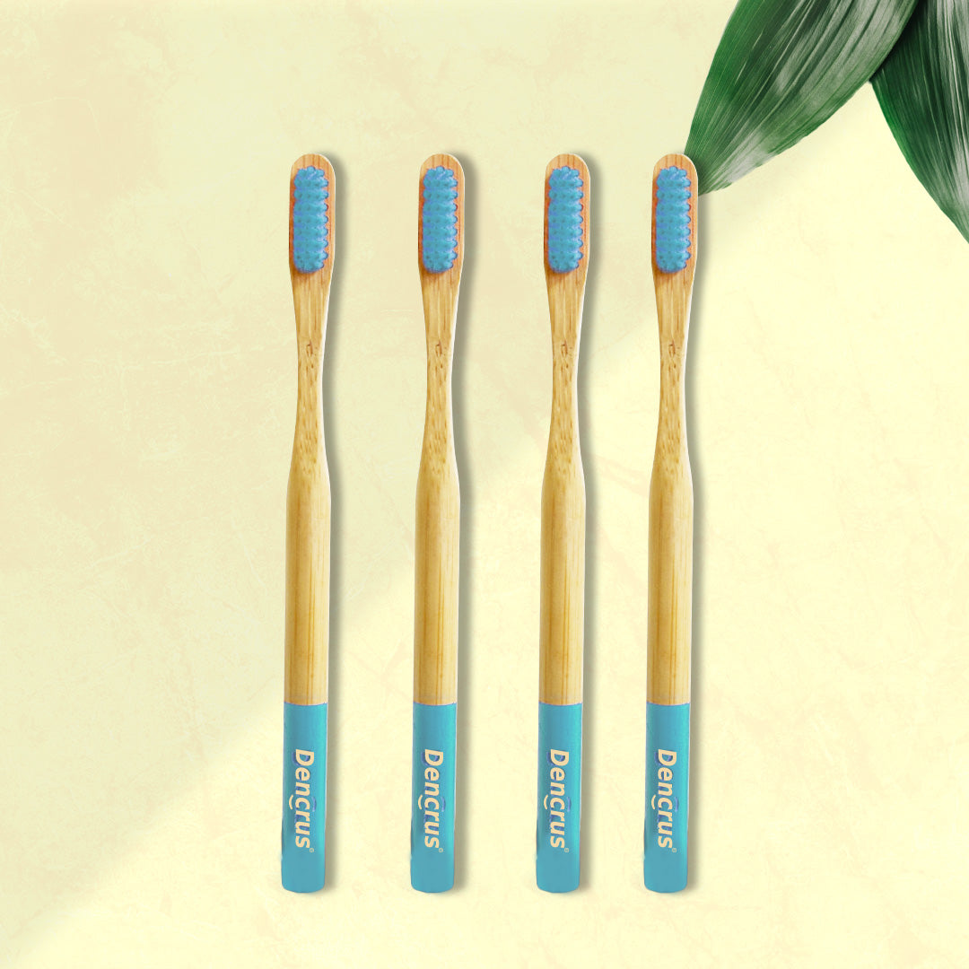 Four ORBY Plus bamboo toothbrushes with blue bristles and bamboo handles, displayed on a beige background with a green leaf to the side.