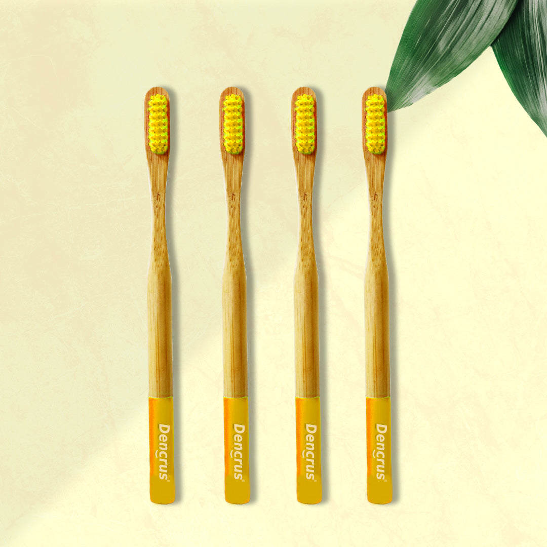Four ORBY Plus yellow bamboo toothbrushes with ergonomic handles, displayed on a beige background with a green leaf to the side.