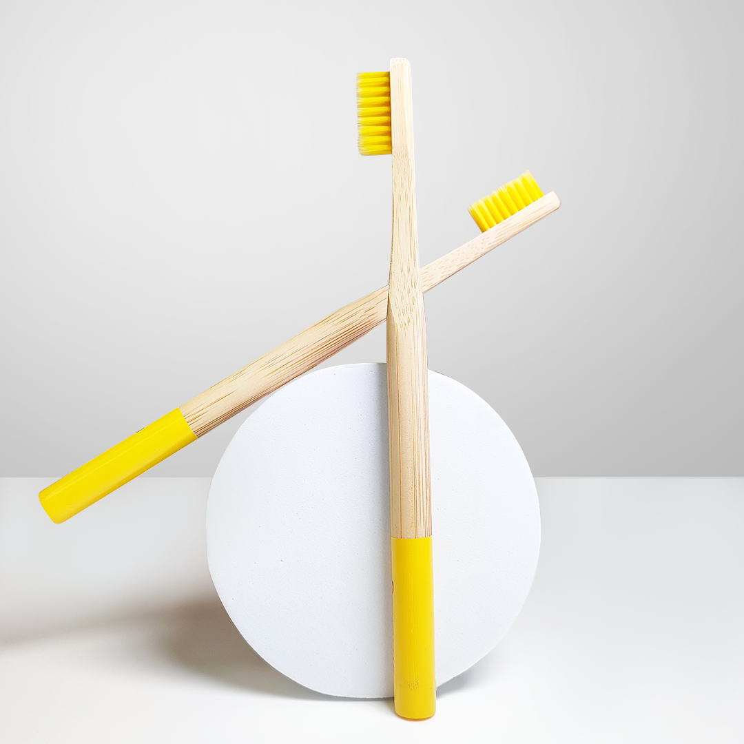 Two ORBY Plus yellow bamboo toothbrush placed on a round white block against a white background 
