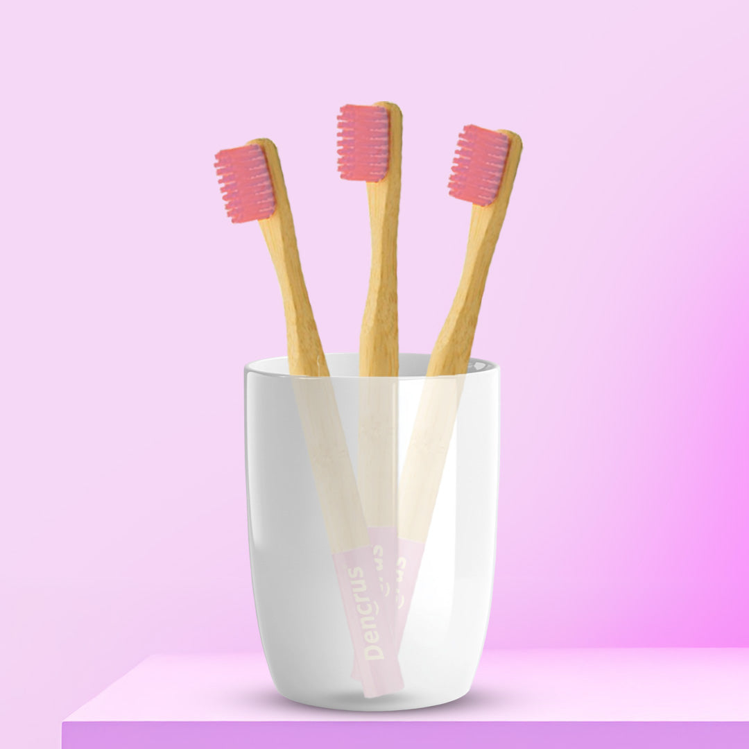 Three pink ORBY Kids bamboo toothbrushes with round handles, placed in a white cup against a pink background.